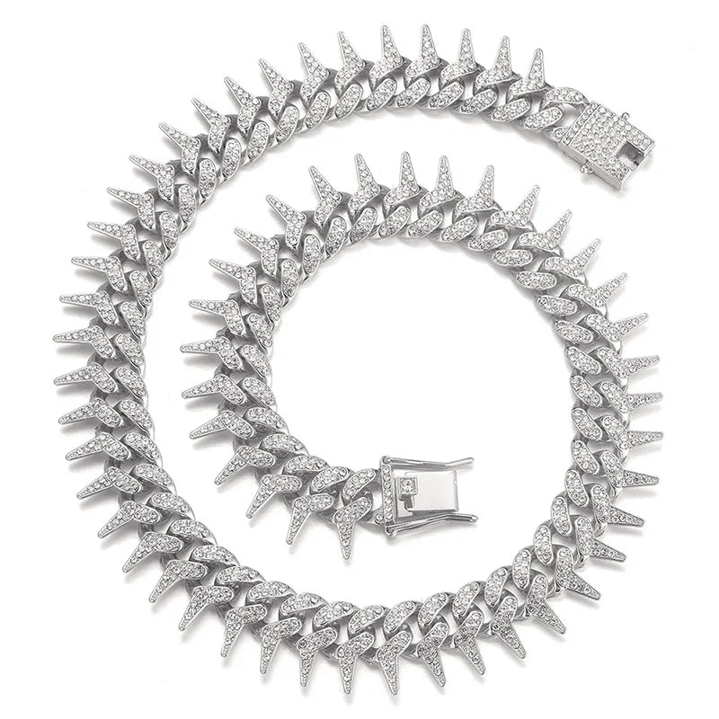 Collier chaîne argenté pour chien avec strass et pointes enroulé sur fond clair.