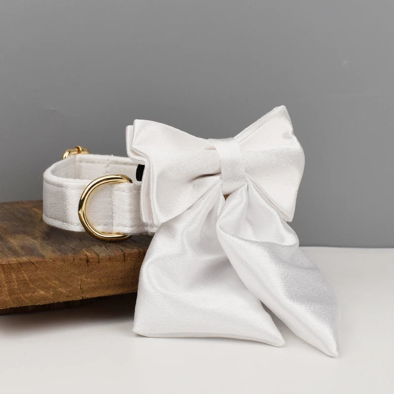 Collier blanc pour chien avec grand nœud détachable et anneau métal doré présenté sur un support en bois.