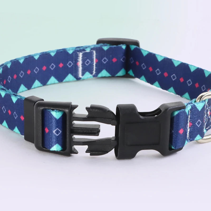 Collier pour chien en nylon bleu marine avec motifs géométriques turquoise et détails roses et mousqueton métal argenté avec boucle cip noir ouverte sur fond clair.