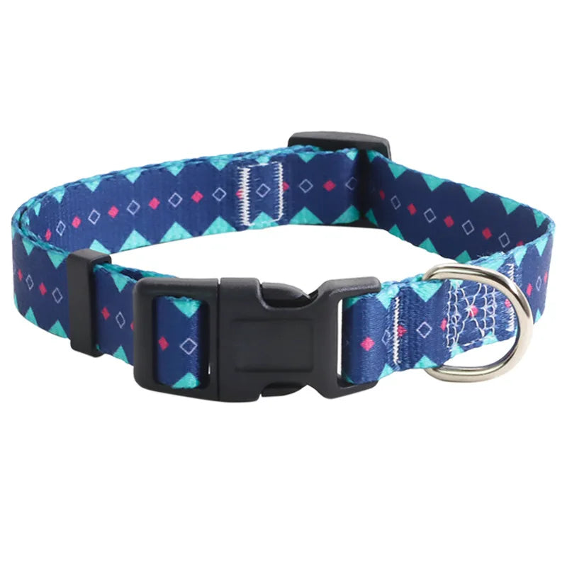 Collier pour chien en nylon bleu marine avec motifs géométriques turquoise et détails roses et mousqueton métal argenté sur fond clair.