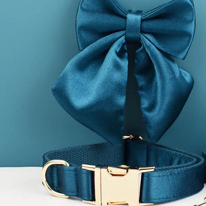 Collier bleu pétrole pour chien avec grand nœud détachable et anneau métal doré présenté devant un fond bleu et blanc.