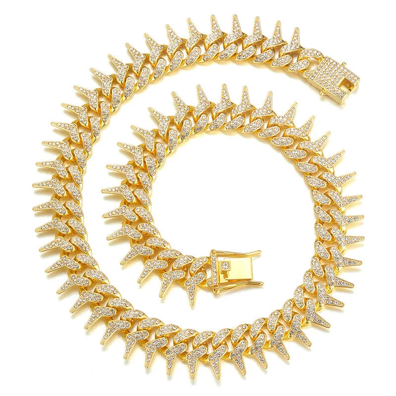 Collier chaîne doré pour chien avec strass et pointes enroulé sur fond clair.