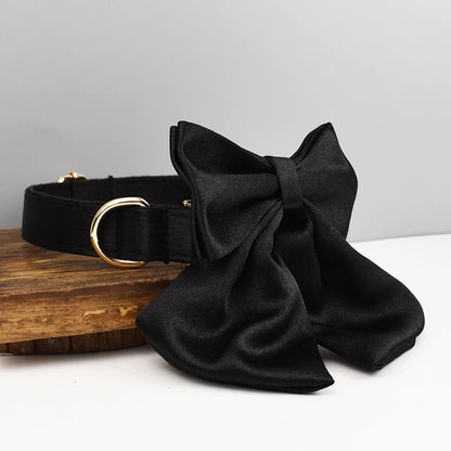 Collier noir pour chien avec grand nœud détachable et anneau métal doré présenté sur un support en bois.