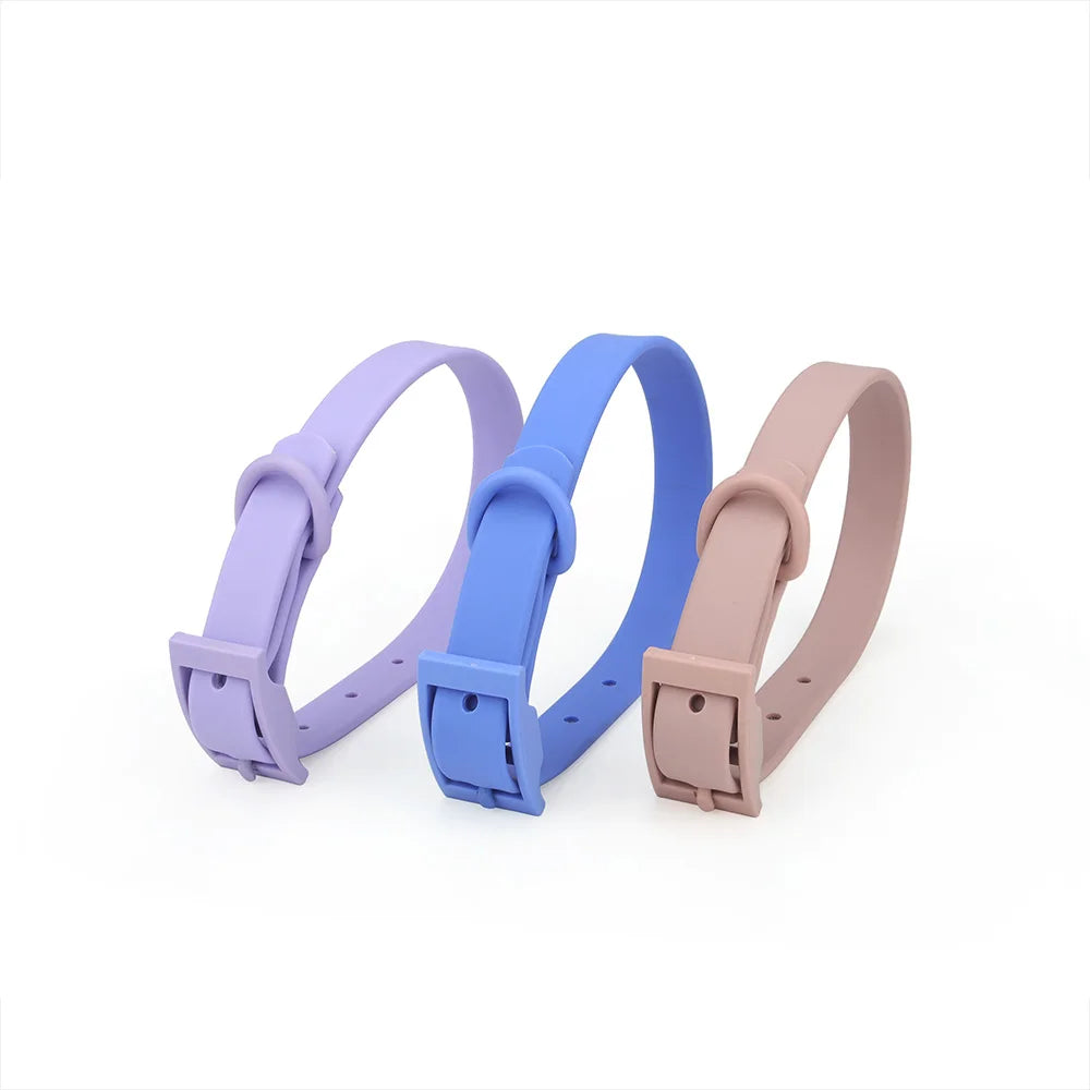 Trois colliers pour chien en PVC imitation silicone présentés côte à côte en coloris lilas, bleu moyen et taupe, avec boucle à ardillon rectangulaire intégrée de même couleur, fond blanc.