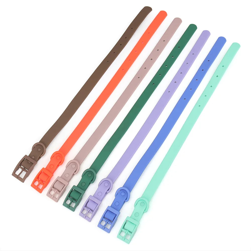 Sept colliers pour chien en PVC imitation silicone posés à plat en éventail sur fond blanc, dans les coloris marron, orange, taupe, vert foncé, lilas, bleu et menthe, boucle à ardillon intégrée visible sur chacun.