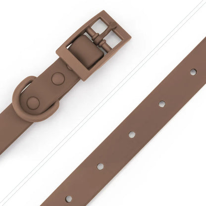 Gros plan sur la boucle à ardillon rectangulaire et l'anneau en D d'un collier chien en PVC imitation silicone marron, avec sangle perforée de trous de réglage bien visible, fond blanc.