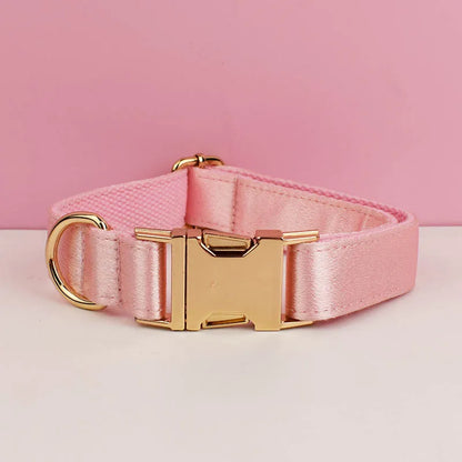 Collier rose pour chien avec boucle métal dorée gravée devant un fond gris et blanc.
