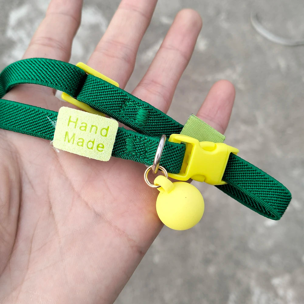 Collier vert pour chiot tenu dans une main avec boule décorative jaune.