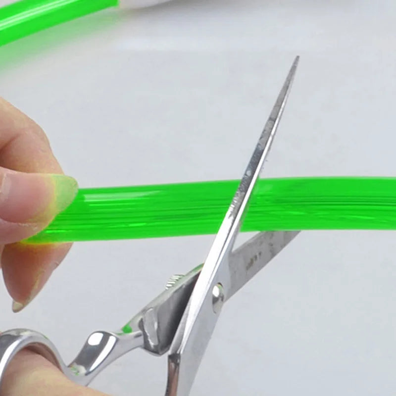 Main tenant un collier lumineux vert pendant une découpe avec des ciseaux.