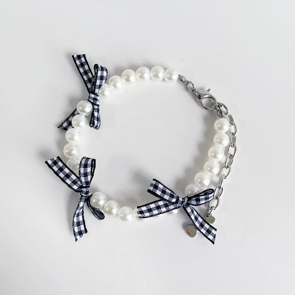 Collier fantaisie pour chiot composé de perles blanches et rubans à carreaux noir et blanc avec chaînette de réglage et mousquetou en métal sur fond clair.