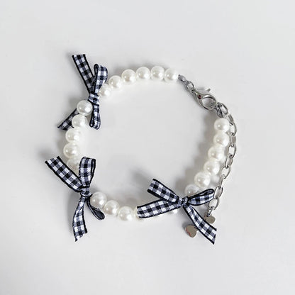 Collier fantaisie pour chiot composé de perles blanches et rubans à carreaux noir et blanc avec chaînette de réglage et mousquetou en métal sur fond clair.