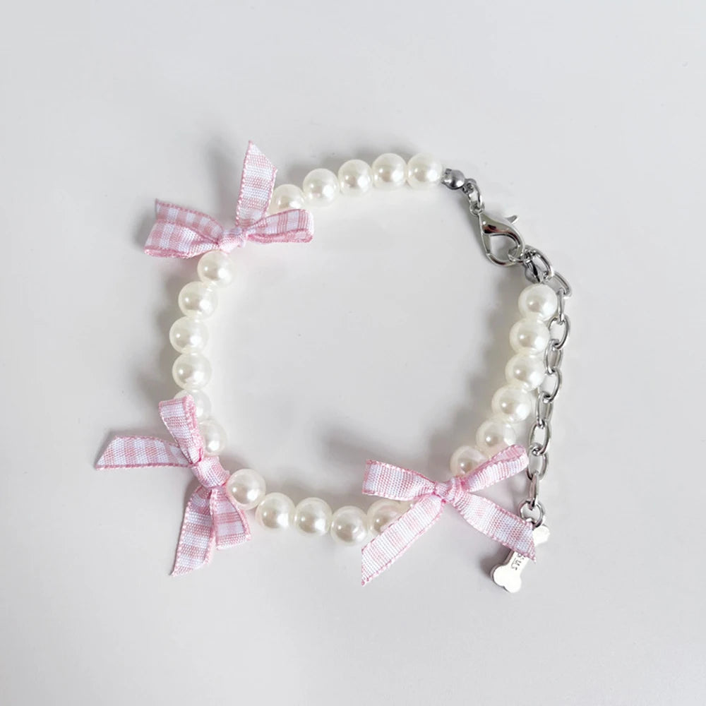 Collier fantaisie pour chiot composé de perles blanches et rubans à carreaux rose et blanc avec chaînette de réglage et mousquetou en métal sur fond clair.