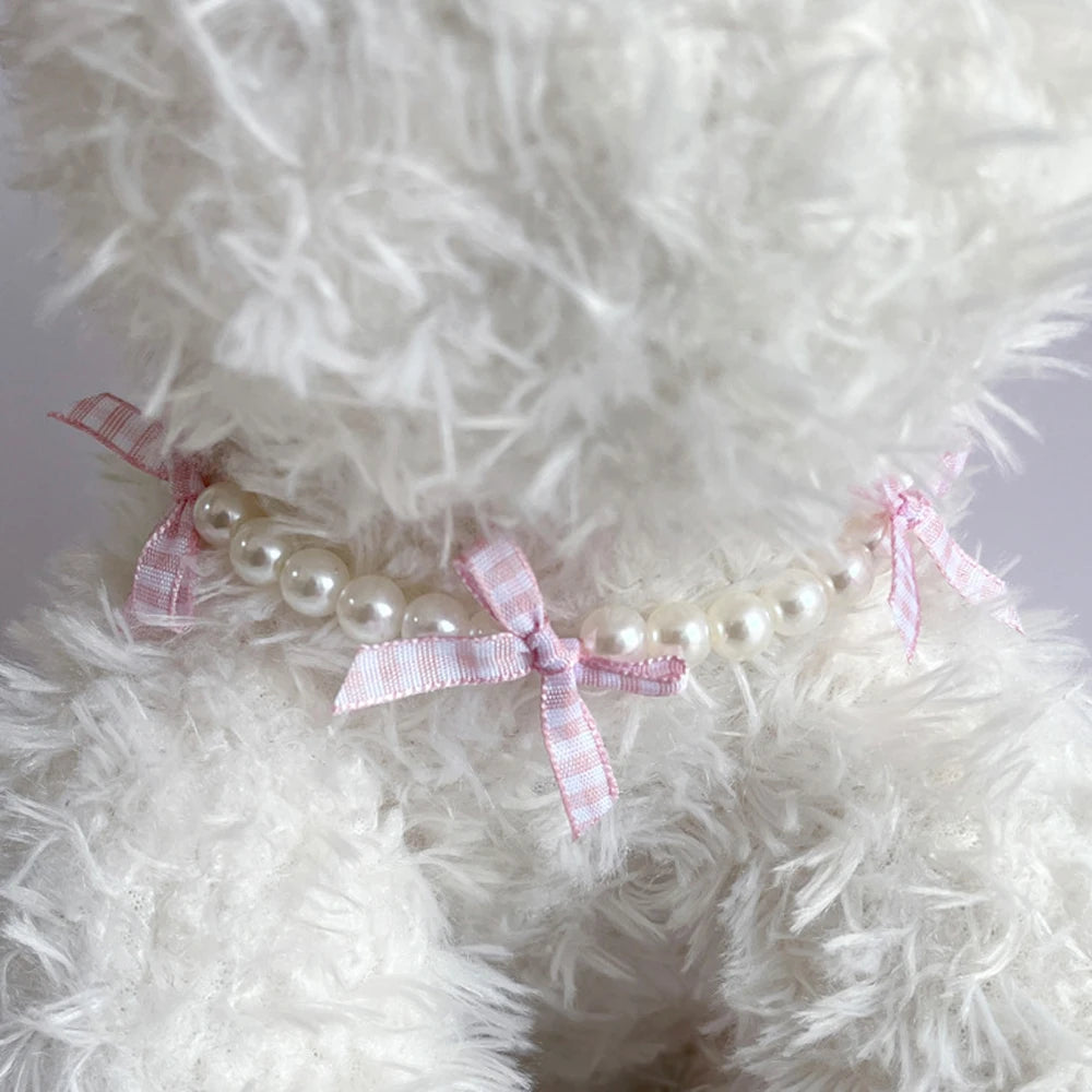 Collier fantaisie pour chiot composé de perles blanches et rubans à carreaux rose pâle photographié autour du cou d'un chiot blanc.