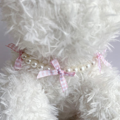 Collier fantaisie pour chiot composé de perles blanches et rubans à carreaux rose pâle photographié autour du cou d'un chiot blanc.