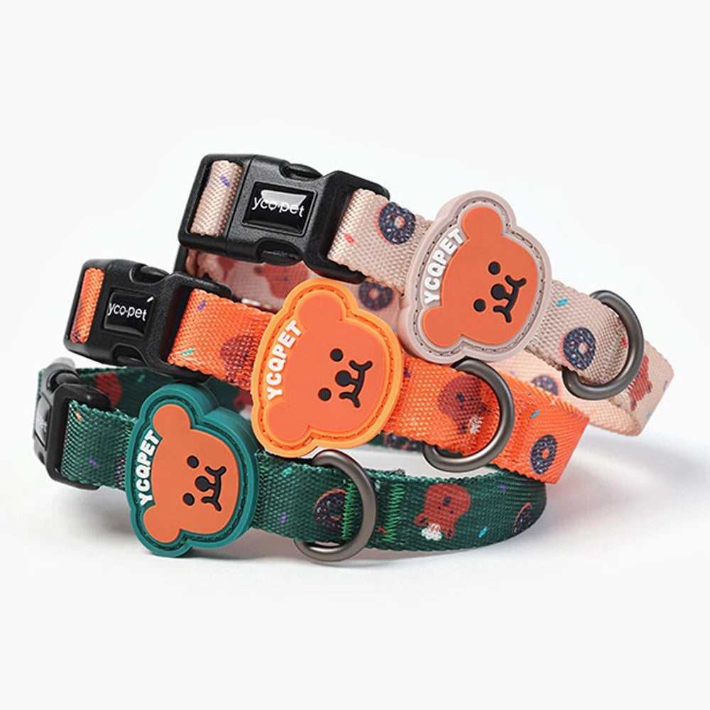 Trois colliers pour chiot empilés en vert, orange et beige clair avec badge ourson sur fond blanc.
