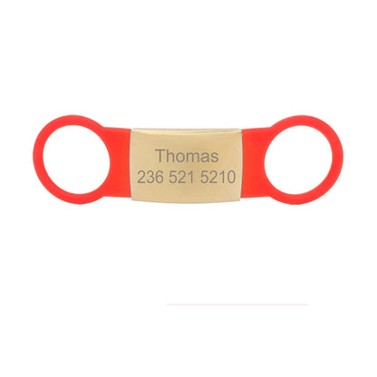 Étiquette rouge pour collier de chien avec plaque dorée gravée Thomas sur fond blanc.