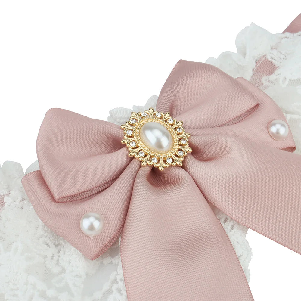 Gros plan sur un nœud rose poudré avec bijou central et perles décoratives sur collier en dentelle blanche pour chien.