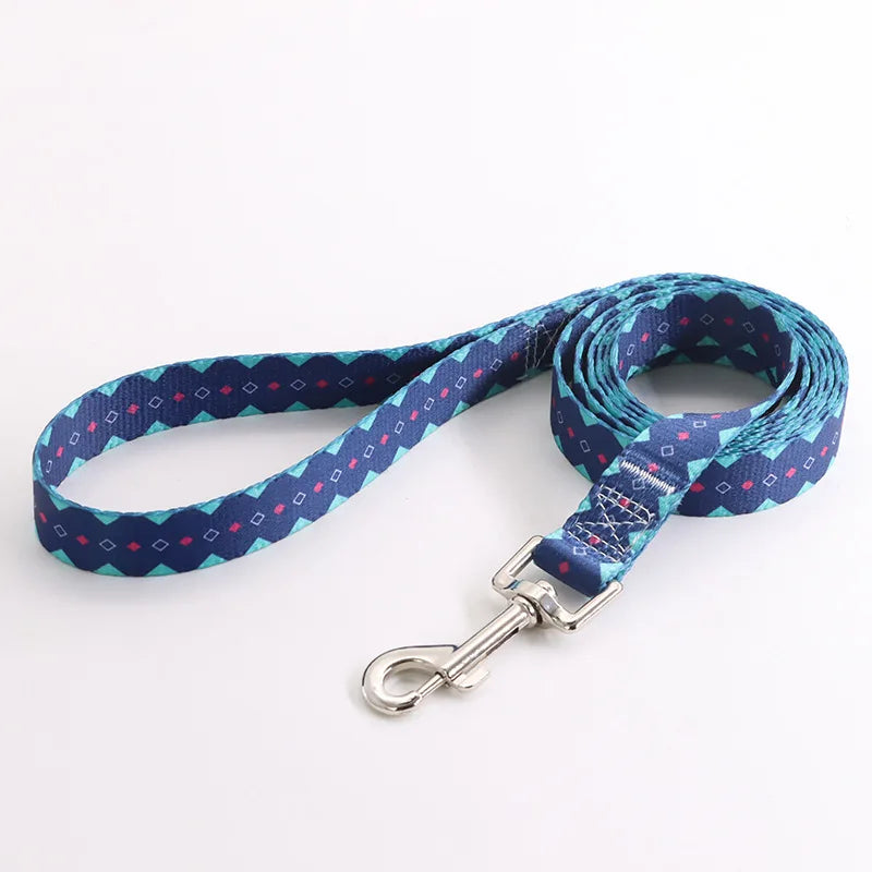 Laisse pour chien en nylon bleu marine avec motifs géométriques turquoise et détails roses et mousqueton métal argenté sur fond clair.