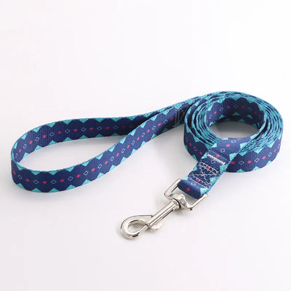 Laisse pour chien en nylon bleu marine avec motifs géométriques turquoise et détails roses et mousqueton métal argenté sur fond clair.