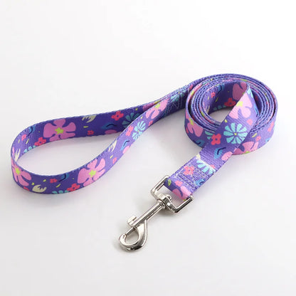 Laisse pour chien en nylon violet avec motifs fleurs roses, bleues et turquoise  et mousqueton métal argenté sur fond clair.