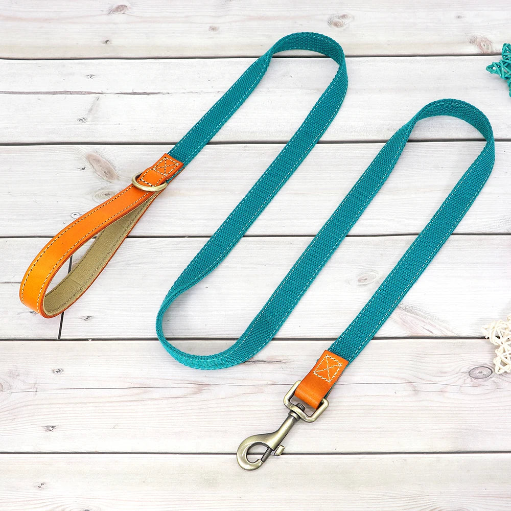 Laisse bleue pour chien avec poignée en cuir orange et mousqueton métal présenté sur un plancher en bois gris dans le fond.