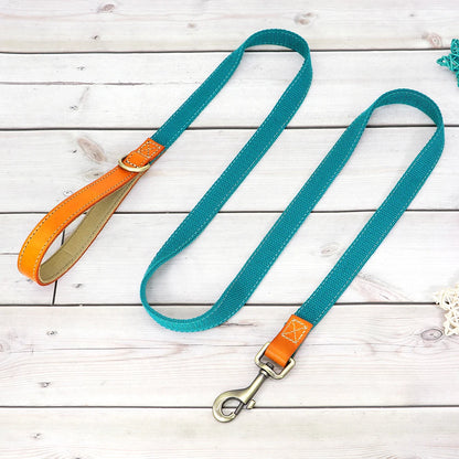 Laisse bleue pour chien avec poignée en cuir orange et mousqueton métal présenté sur un plancher en bois gris dans le fond.