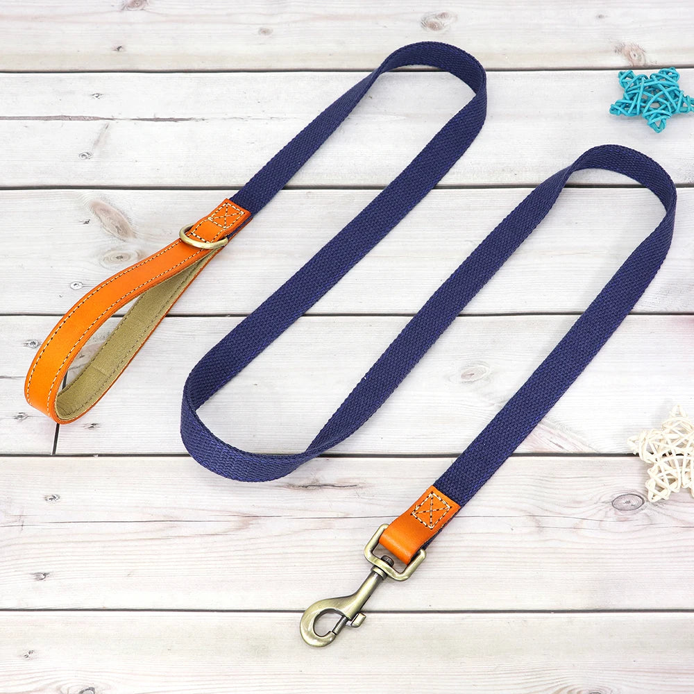 Laisse bleue pour chien avec poignée en cuir orange et mousqueton métal présenté sur un plancher en bois gris dans le fond.