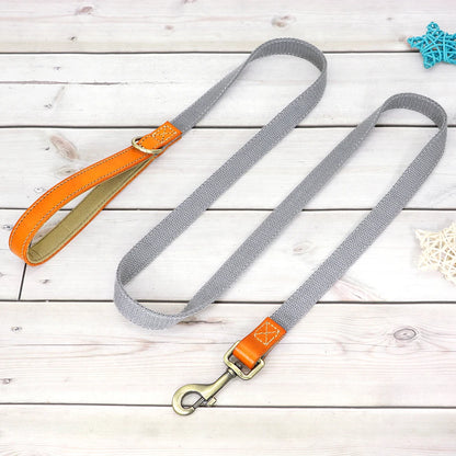 Laisse grise pour chien avec poignée en cuir orange et mousqueton métal présenté sur un plancher en bois gris dans le fond.