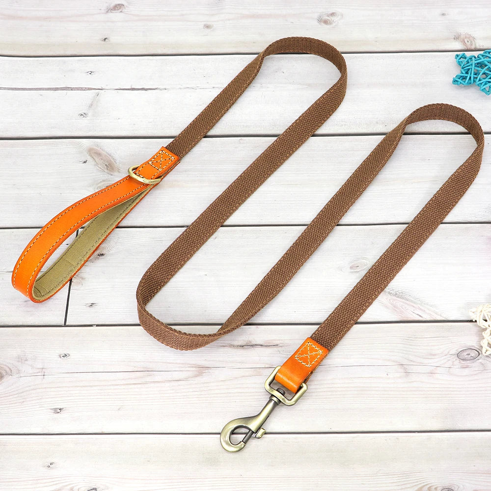 Laisse marron pour chien avec poignée en cuir orange et mousqueton métal présenté sur un plancher en bois gris dans le fond.