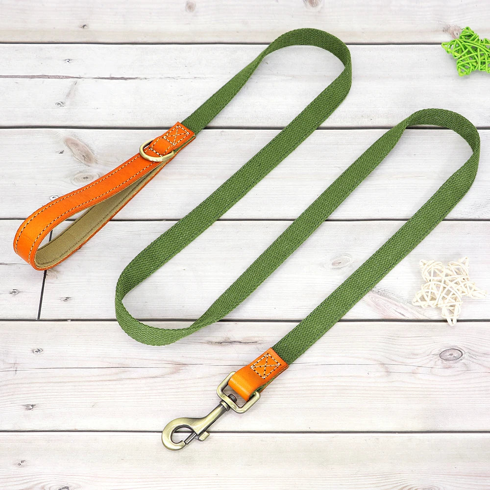 Laisse verte pour chien avec poignée en cuir orange et mousqueton métal présenté sur un plancher en bois gris dans le fond.