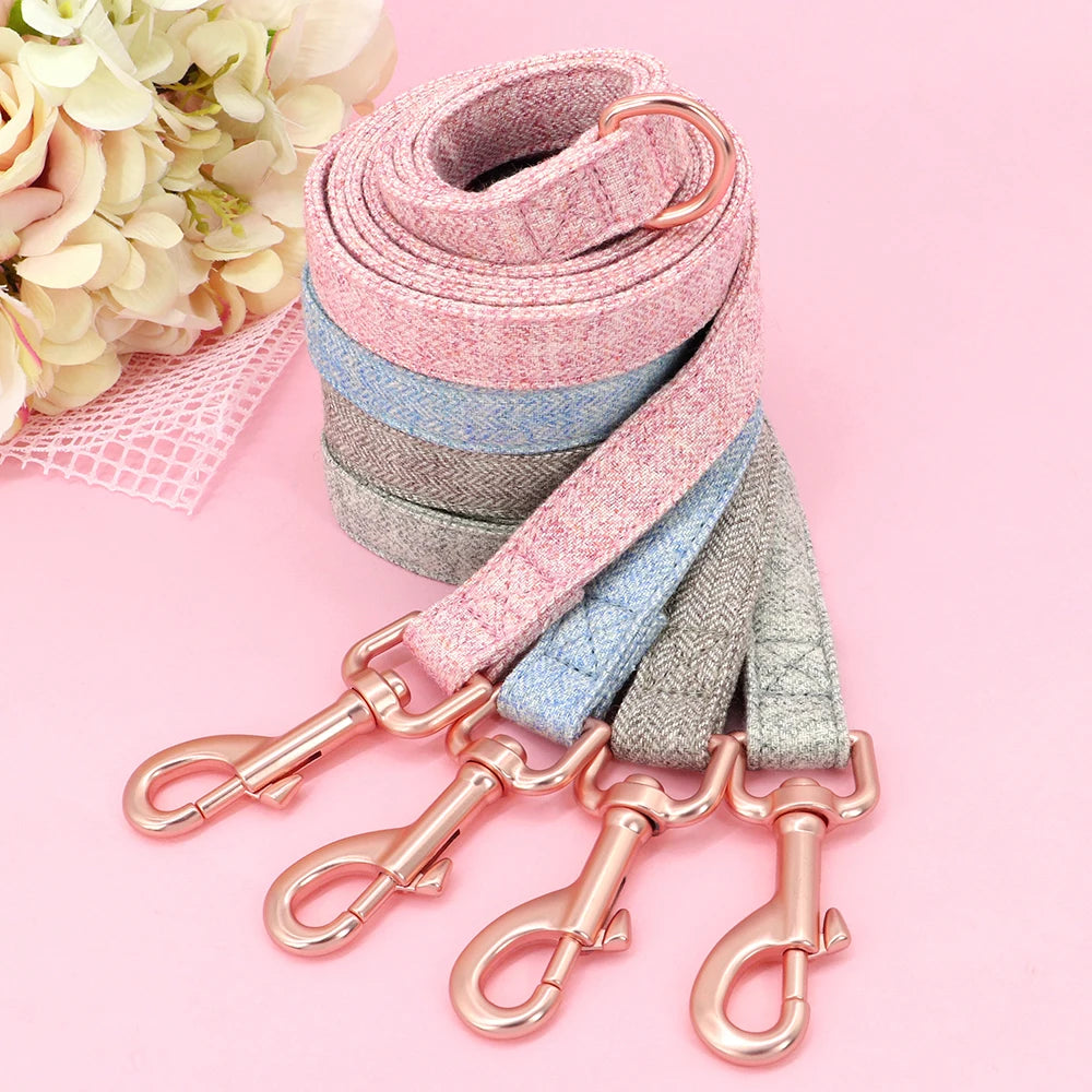Collection de laisses pour chien en rose gris et bleu enroulés et empilés sur fond rose.