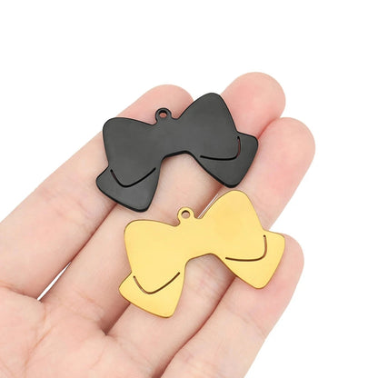Deux pendentifs nœud papillon noir et doré présentés dans une main.