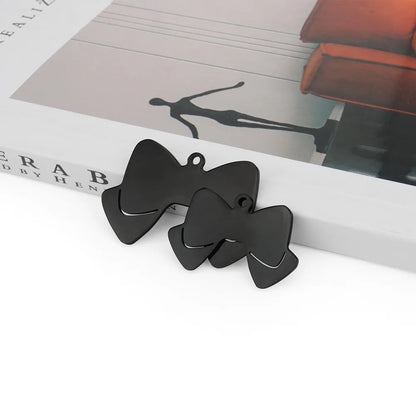 Deux pendentifs noirs en forme de nœud papillon posés sur un support.