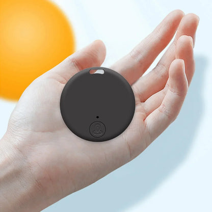Traceur Bluetooth anti-perte rond noir posé dans une paume de main, illustrant sa taille compacte, œillet de fixation et bouton de localisation visibles sur fond clair.
